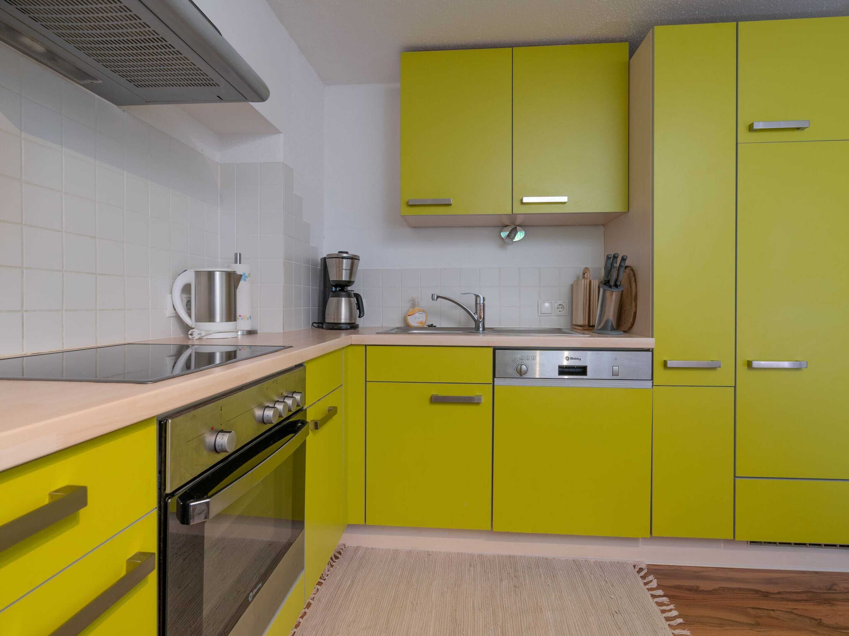 Cocina con armarios amarillos, estufa de acero inoxidable, lavavajillas y cafetera.