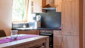Een kleine keuken met houten kastjes, een ingebouwde oven, een magnetron en een raam voor natuurlijk licht.