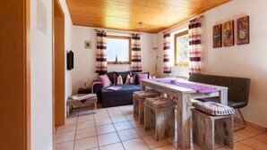 Een gezellige kamer met een houten plafond, een bank, een eettafel met krukken en gestreepte gordijnen.