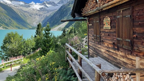 Een houten hut met een balkon met uitzicht op een meer en bergen.