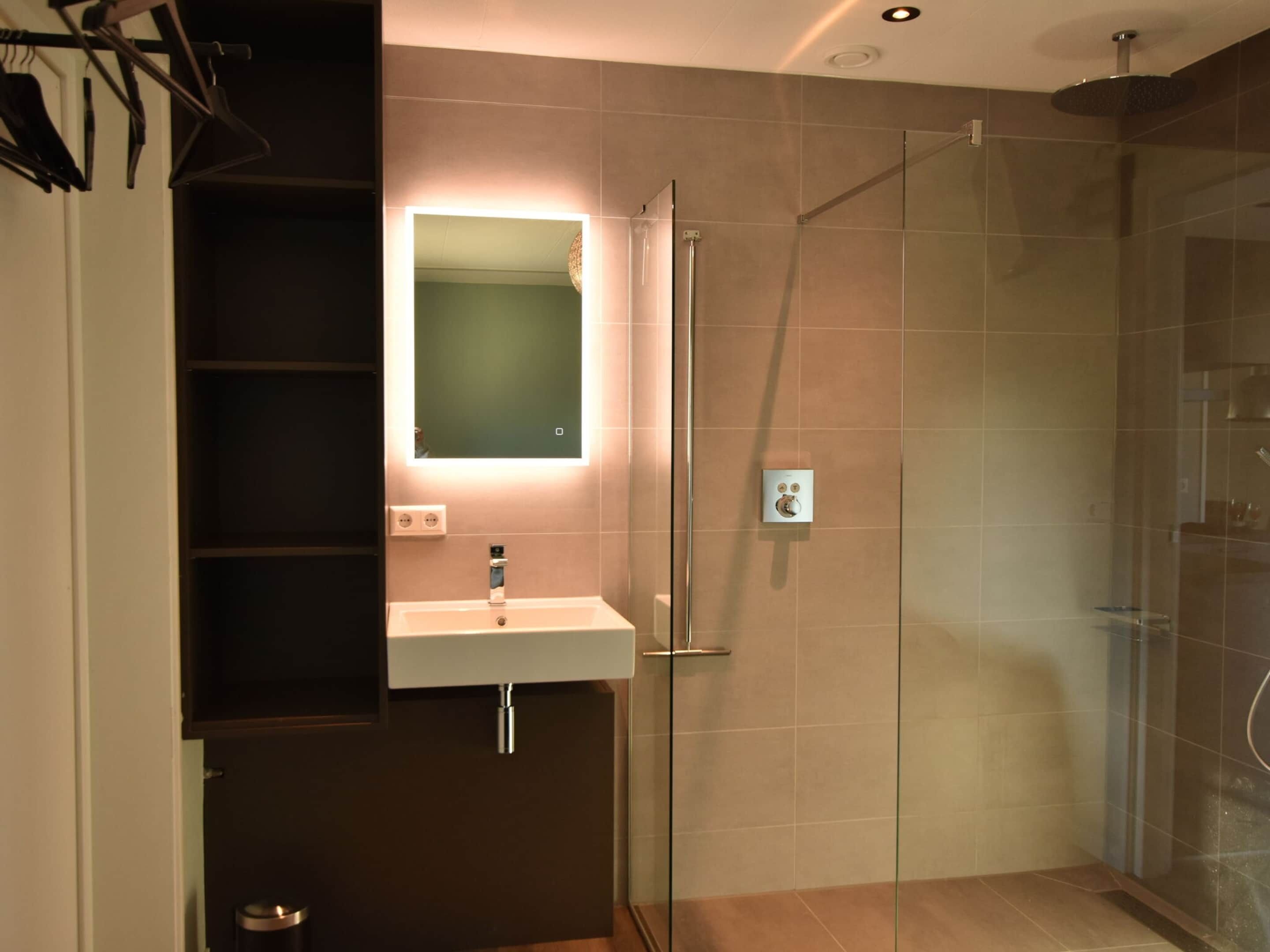 A modern bathroom with a glass shower enclosure, a built-in sink, and a mirror with backlighting.