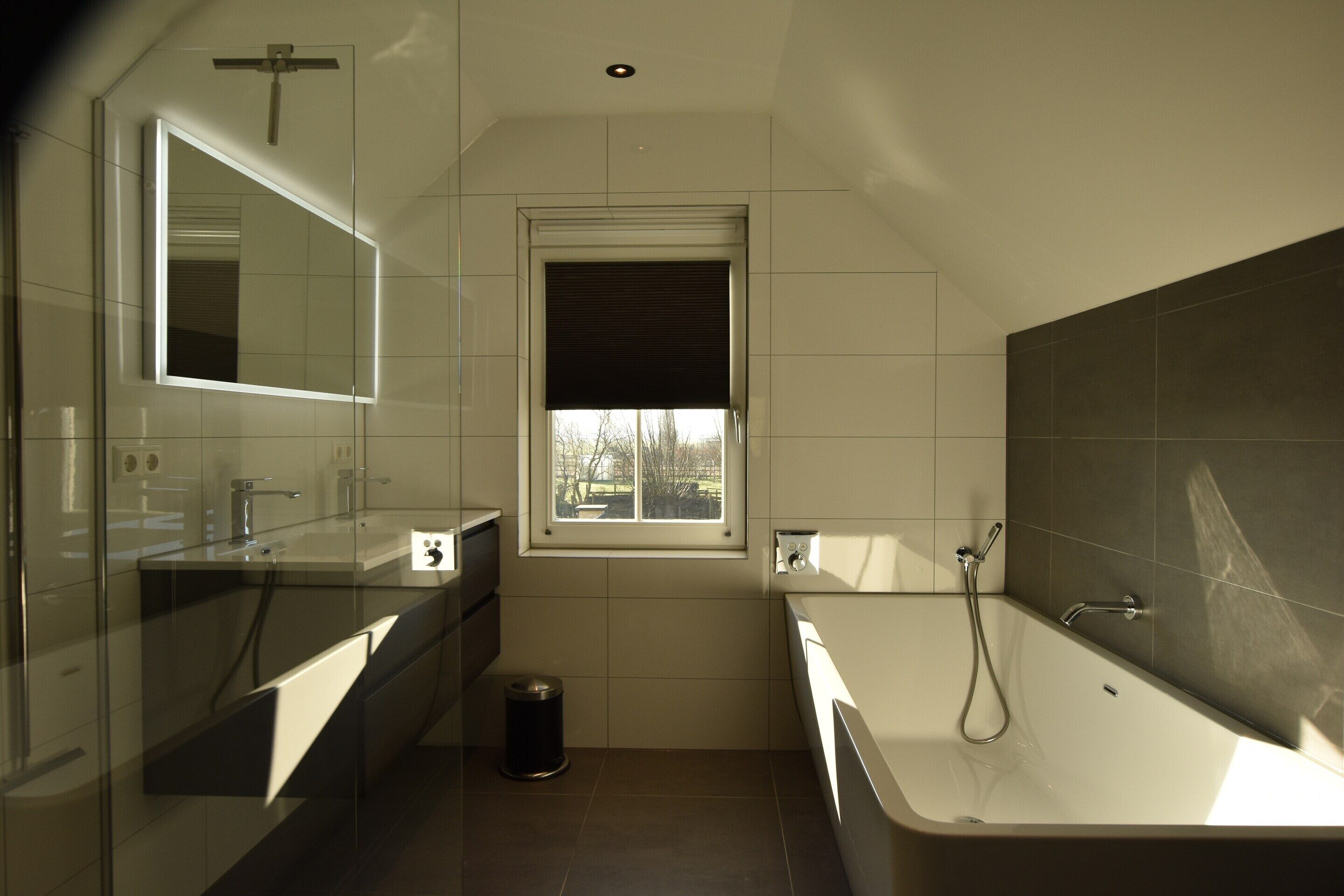 A modern bathroom with a glass shower enclosure, a large mirror, and a bathtub.