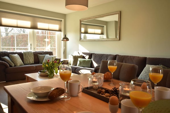 A dining area with a wooden table set for breakfast, including bowls, glasses of orange juice, and pastries.