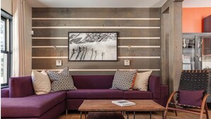 A modern living room with a purple sectional sofa, a wooden coffee table, and a framed photograph on the wall.