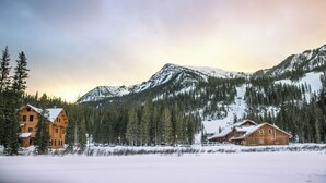 A wooden lodge with a snow-covered landscape and mountains in the background. - Bavarian Chalet 1 - Bavarian-inspired chalet with stylish decor and easy ski acc (Taos Ski Valley)