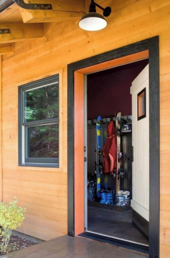 Una cabaña de madera con una puerta que da a un área de almacenamiento donde hay esquíes y tablas de snowboard.