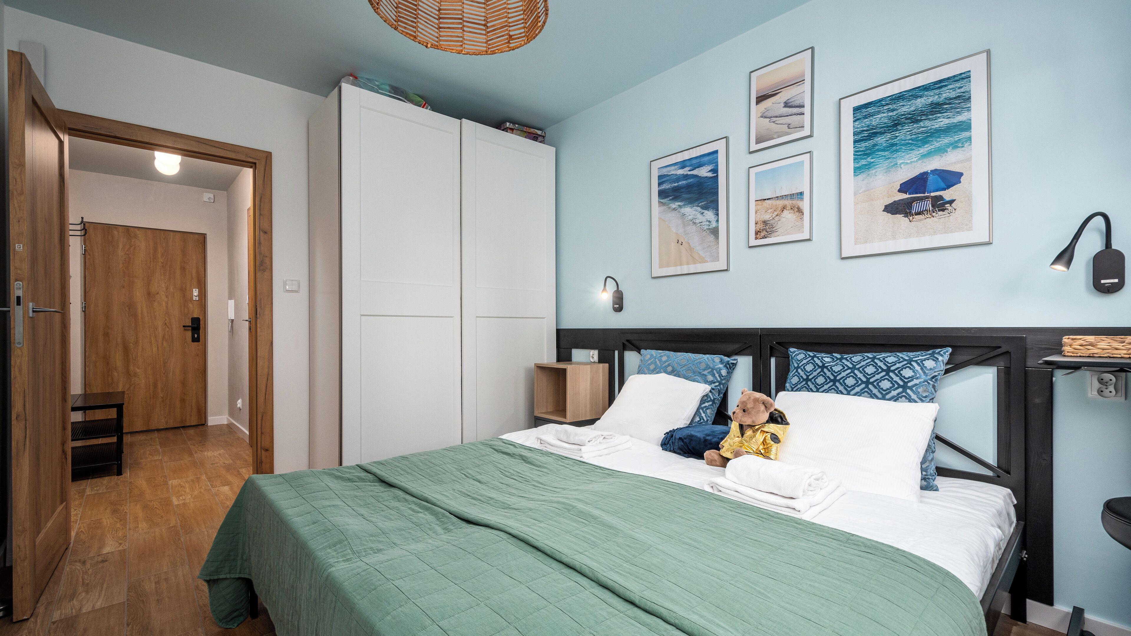 A bedroom with a bed, a nightstand, a wall-mounted lamp, and a door leading to another room.