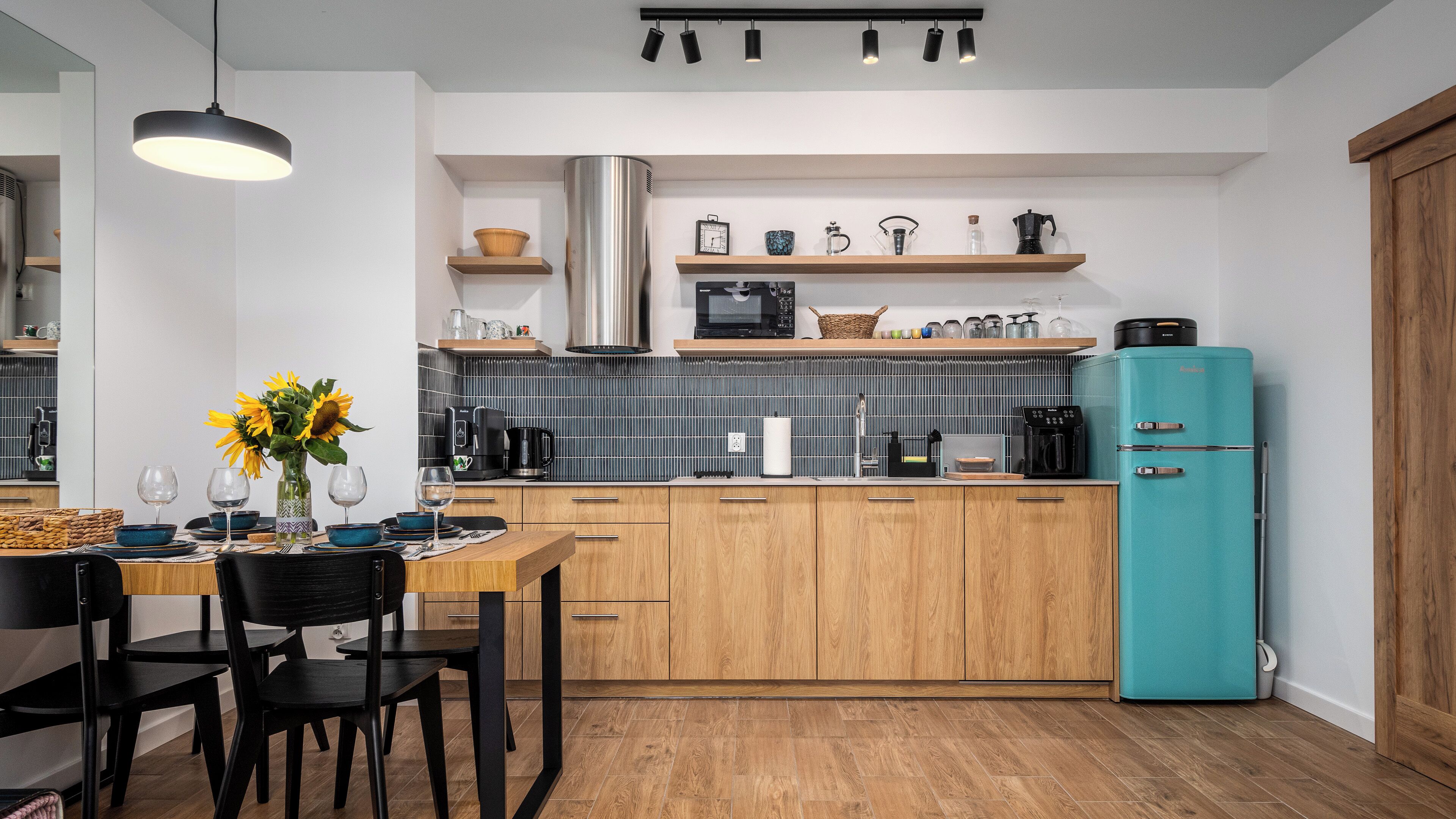 A modern kitchen with wooden cabinets, a teal refrigerator, and a dining area with a table set for two.