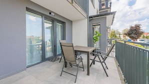 An outdoor balcony with a table and chairs, a potted plant, and a view of the street. - Apartamenty Sun & Snow Nad Ujściem (Leba)
