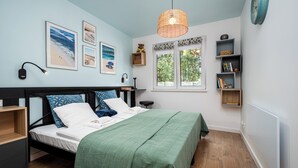 A bedroom with a bed, a bedside table, a window with a view, wall-mounted shelves, and framed pictures. - Apartamenty Sun & Snow Nad Ujściem (Leba)