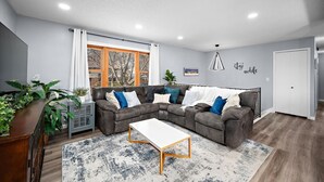 Un salon moderne avec un canapé d’angle, une table basse et une grande fenêtre agrémentée de rideaux.