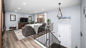 Un salon moderne avec un canapé gris, un téléviseur à écran plat et un escalier menant à un niveau supérieur.
