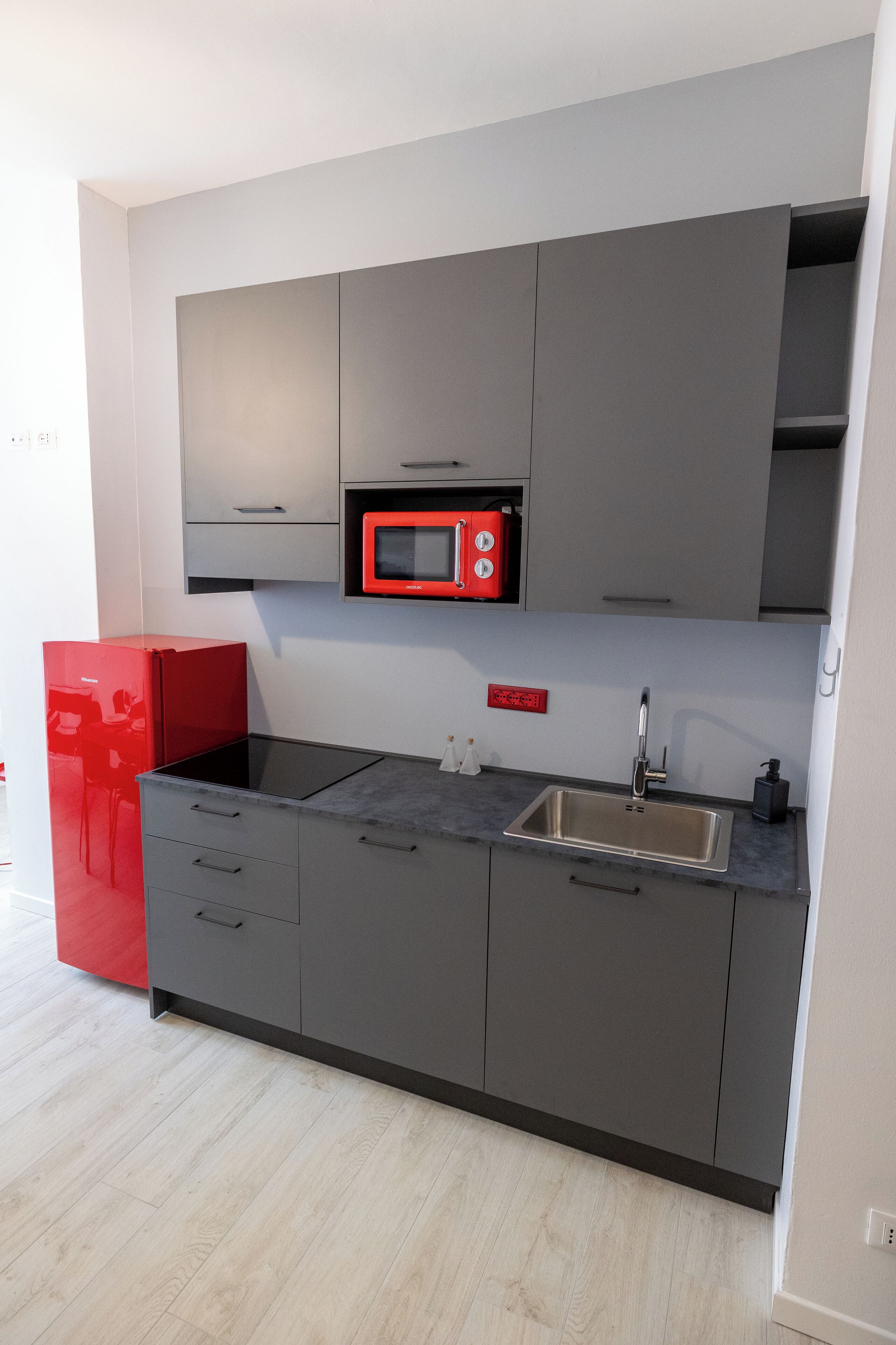 Une cuisine moderne avec des meubles gris, un réfrigérateur rouge et un évier en acier inoxydable.