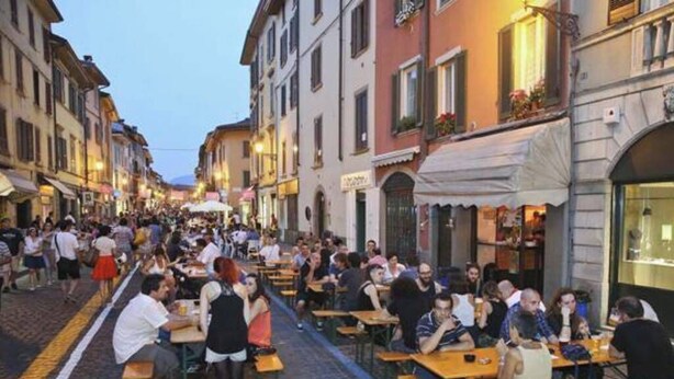 A cobblestone street lined with buildings, outdoor seating areas, and people dining. - Cà Cianfer (Bergamo)