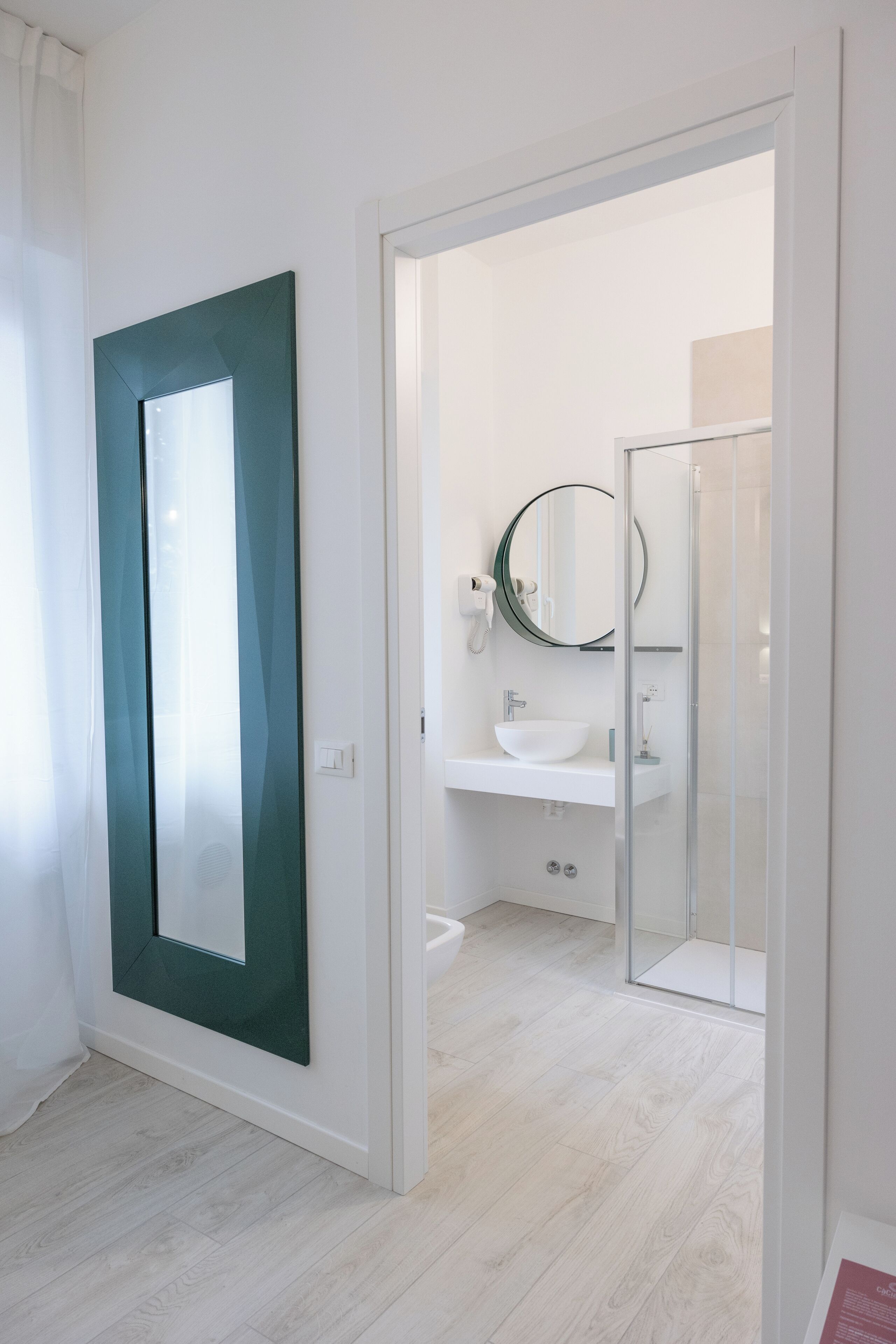 A modern bathroom with a white sink, a round mirror, and a glass shower enclosure.