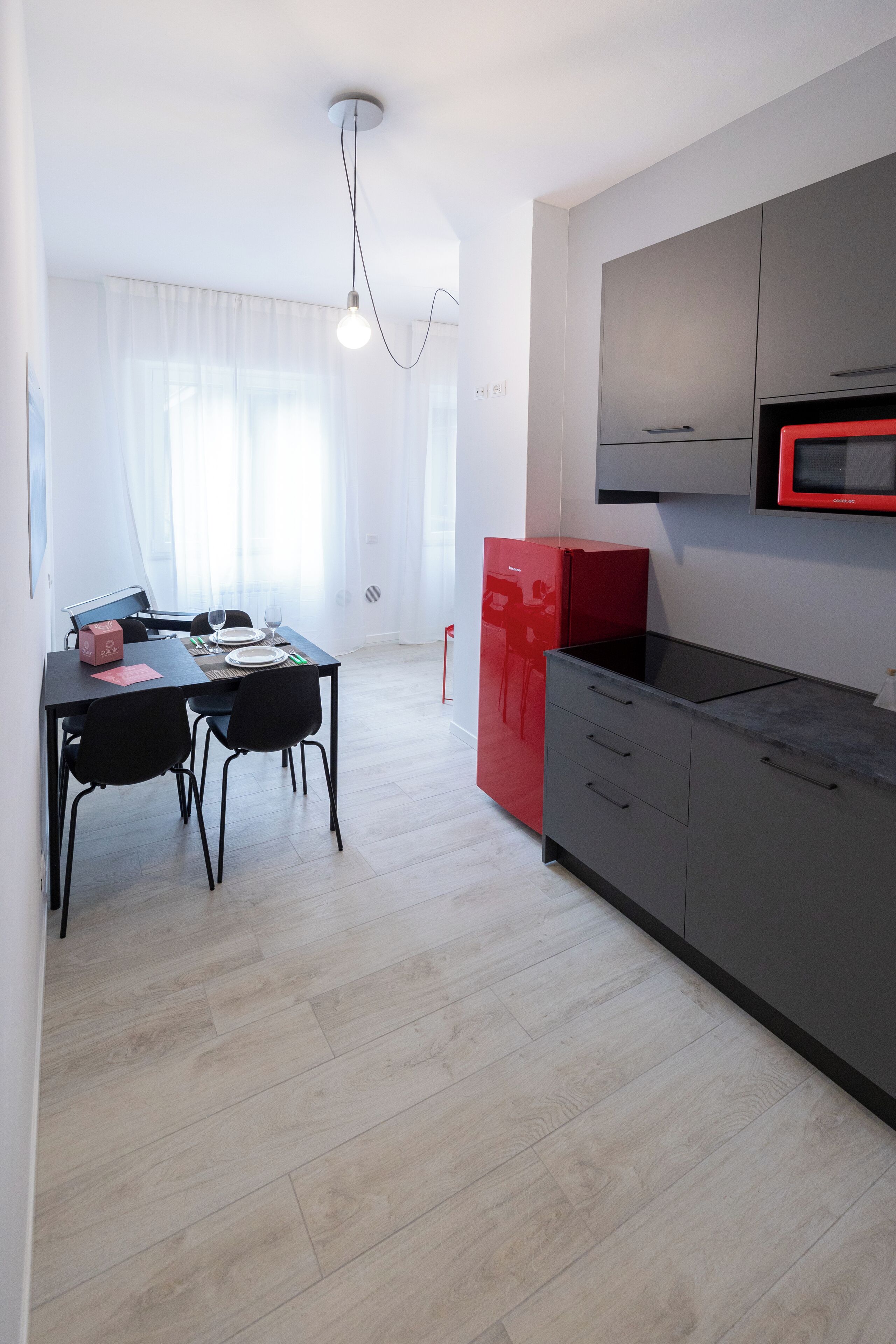 A modern kitchen with grey cabinets, a red refrigerator, and a dining area with a table and chairs.