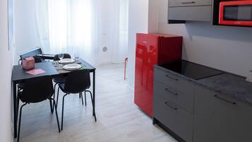 A modern kitchen with grey cabinets, a red refrigerator, and a dining area with a table and chairs.