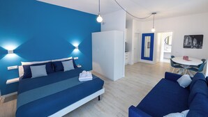 A modern bedroom with a bed, a blue sofa, a dining table, and a kitchen area. - Cà Cianfer (Bergamo)