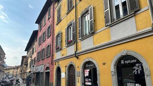 A street view with a yellow building featuring a shop with a sign reading "epilate" and a price of 19€. - Cà Cianfer (Bergamo)