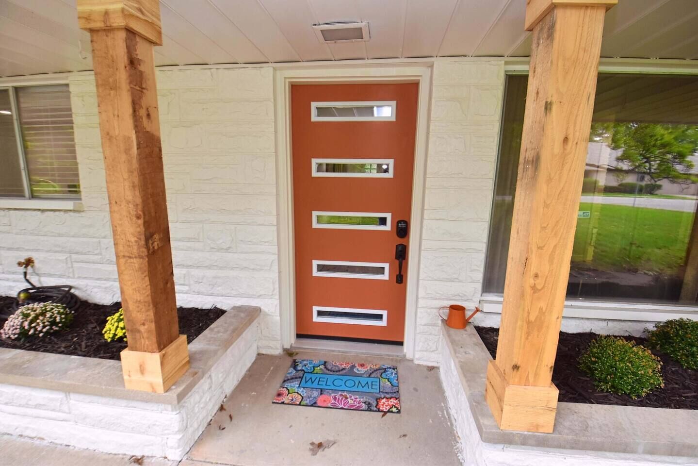 Una puerta principal con felpudo, columnas de madera y un muro de ladrillo.