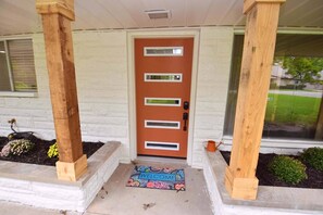 Una puerta principal con felpudo, columnas de madera y un muro de ladrillo.