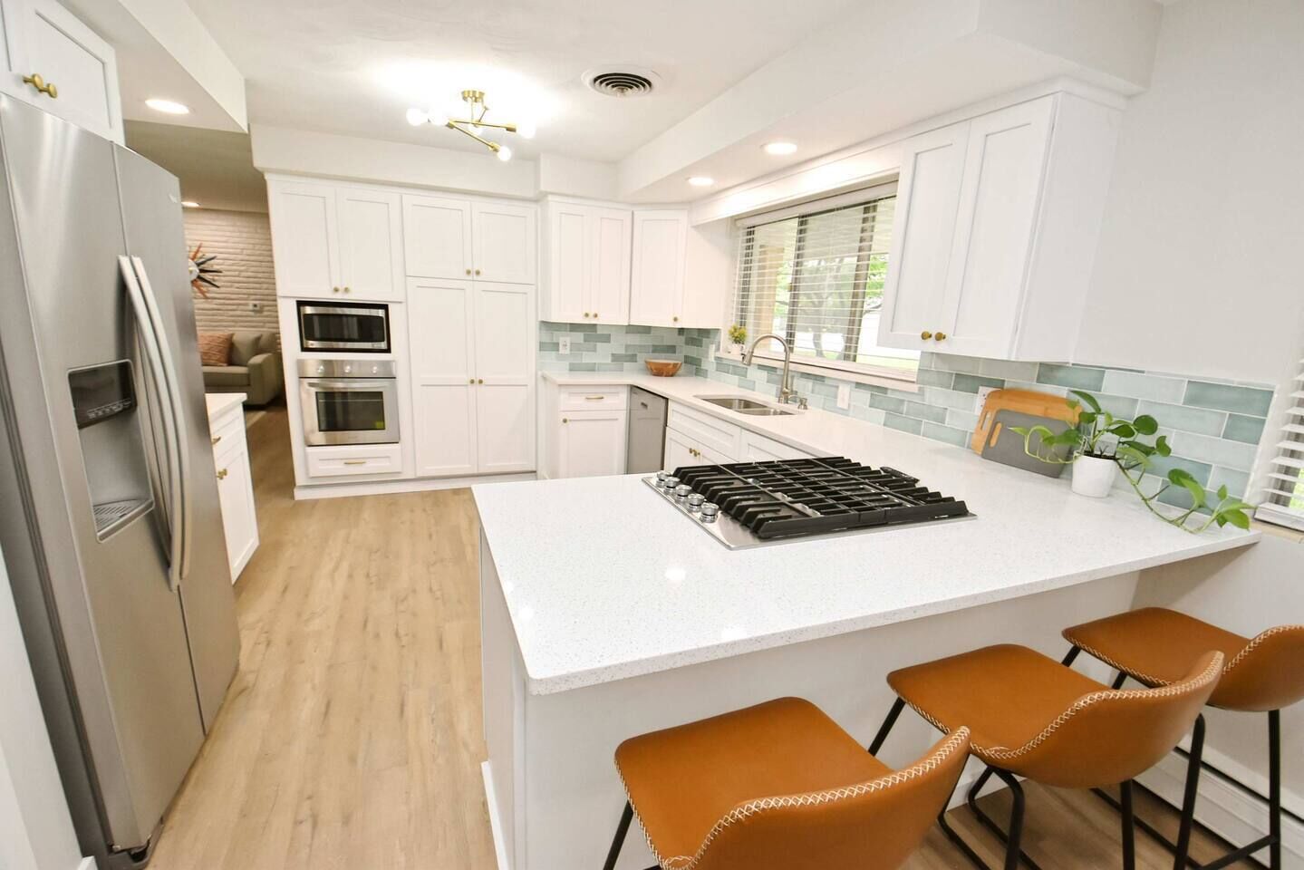 A modern kitchen with white cabinetry, a stainless steel refrigerator, a built-in oven, a gas stove, and a large island with bar stools.