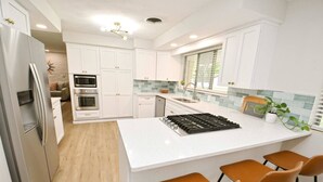 A modern kitchen with white cabinetry, a stainless steel refrigerator, a built-in oven, a gas stove, and a large island with bar stools. - Mid Century Modern, 10 min walk to ND! (1831) (South Bend)