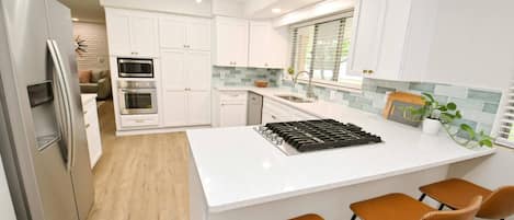 A modern kitchen with white cabinetry, a stainless steel refrigerator, a built-in oven, a gas stove, and a large island with bar stools.