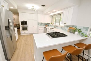 A modern kitchen with white cabinetry, a stainless steel refrigerator, a built-in oven, a gas stove, and a large island with bar stools.