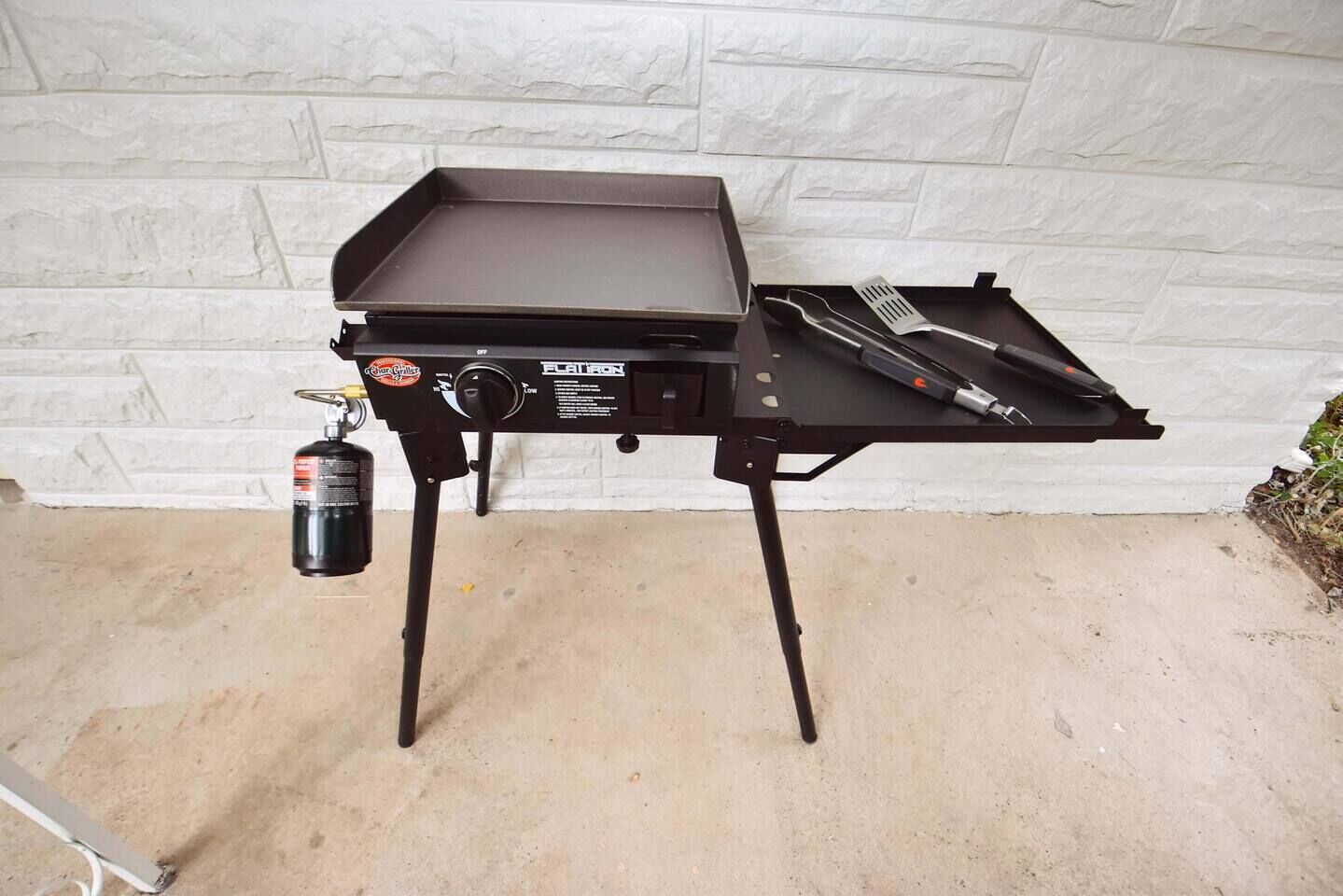 Un barbecue portable doté d’une surface de cuisson plane et d’un brûleur latéral, équipé d’une bouteille de propane.