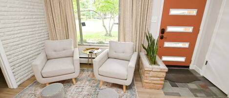 A room with two armchairs, a small table, a patterned rug, a potted plant, and a door with frosted glass panels.