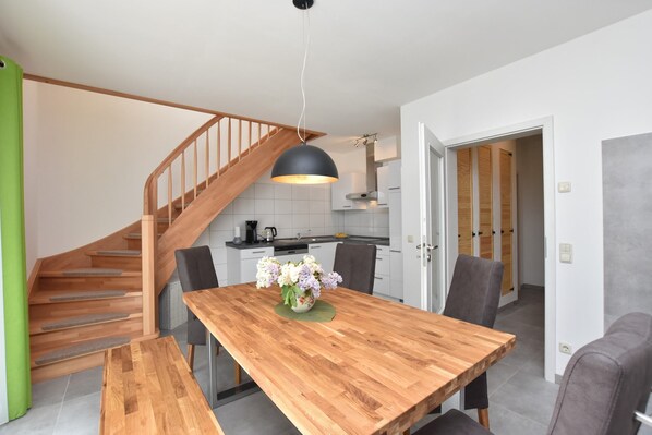 Eine moderne Küche mit einer Holztreppe, einem Esstisch mit Stühlen und einer Pendelleuchte.