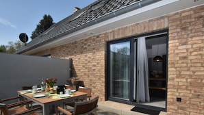 A patio with a table set for dining, a brick wall, and a sliding glass door leading to an interior space. - Idyllic Holiday Home in Damshagen With Terrace (Damshagen)