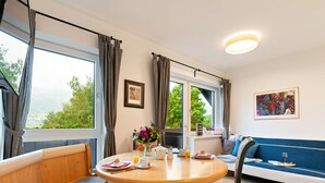 A cozy room with a wooden dining table, benches, a sofa, and large windows offering a view of greenery. - Spacious Apartment in Katschberg (Sankt Michael im Lungau)