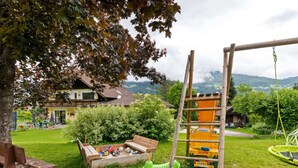 A playground with a swing set and a climbing structure, surrounded by a grassy area with a bench and a sandbox. - Spacious Apartment in Katschberg (Sankt Michael im Lungau)