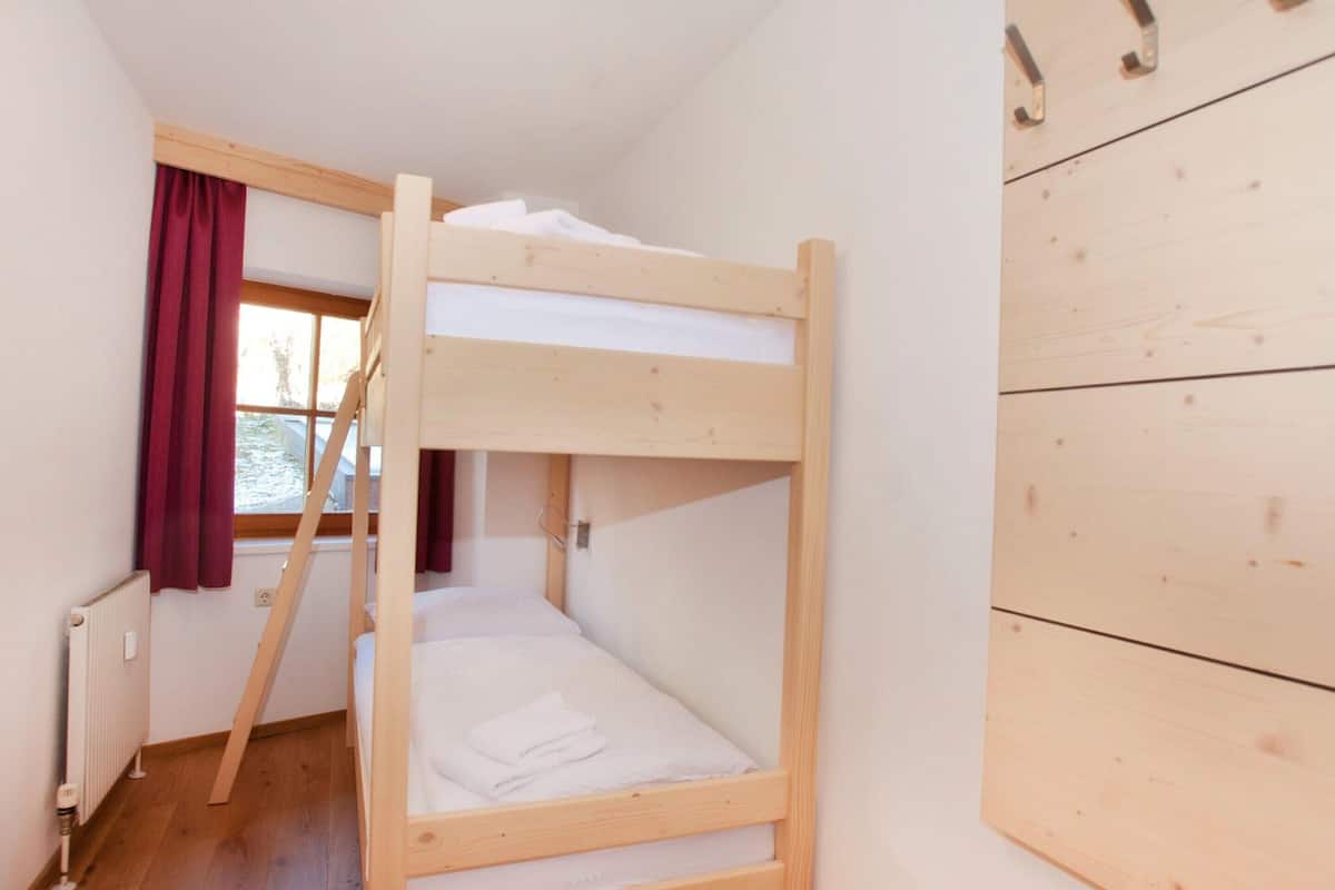 A bunk bed room with a window, a radiator, and a wooden wall.