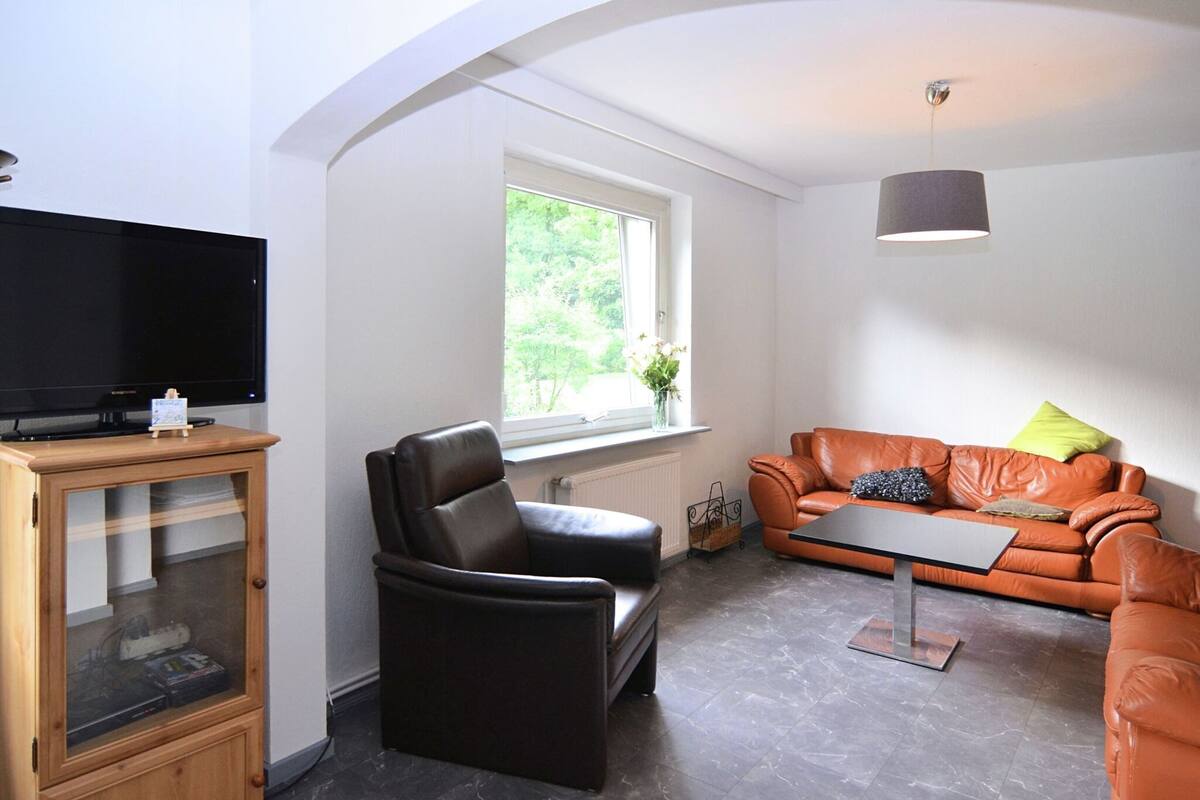 Una sala de estar moderna con un sofá de cuero, un sillón negro y un mueble de madera con un televisor encima.