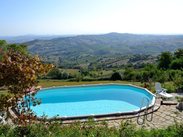 A rectangular swimming pool with a clear blue water surface, surrounded by a stone deck. In the background, there is a view of rolling hills and a clear sky.