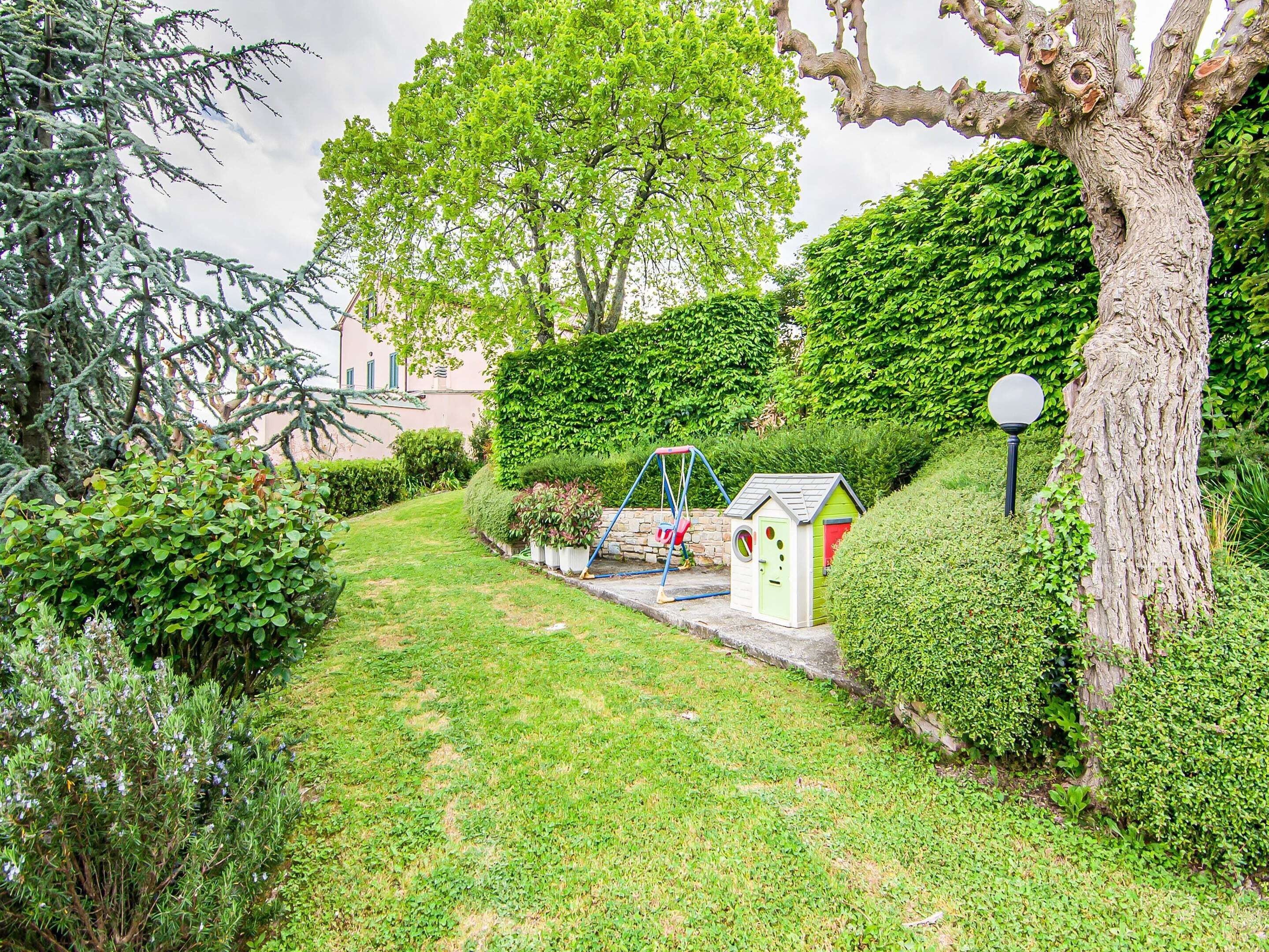 A well-maintained garden with a swing set, a small playhouse, and a large tree.