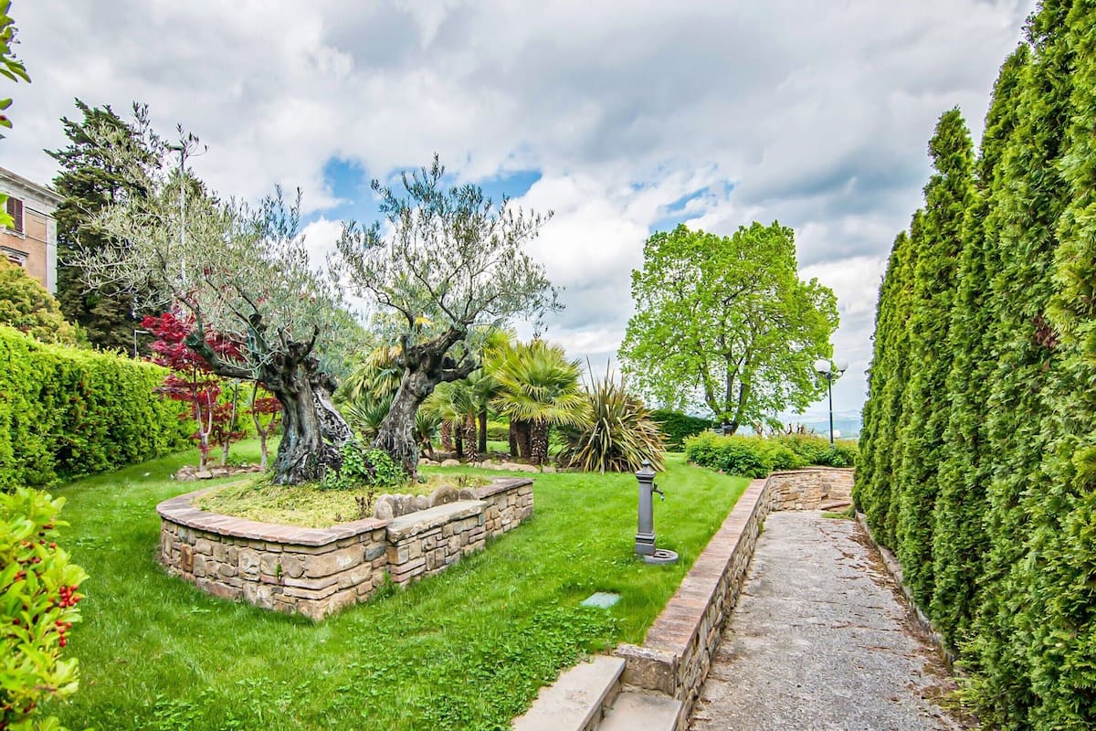 A well-maintained garden with a stone pathway, various shrubs, and trees.