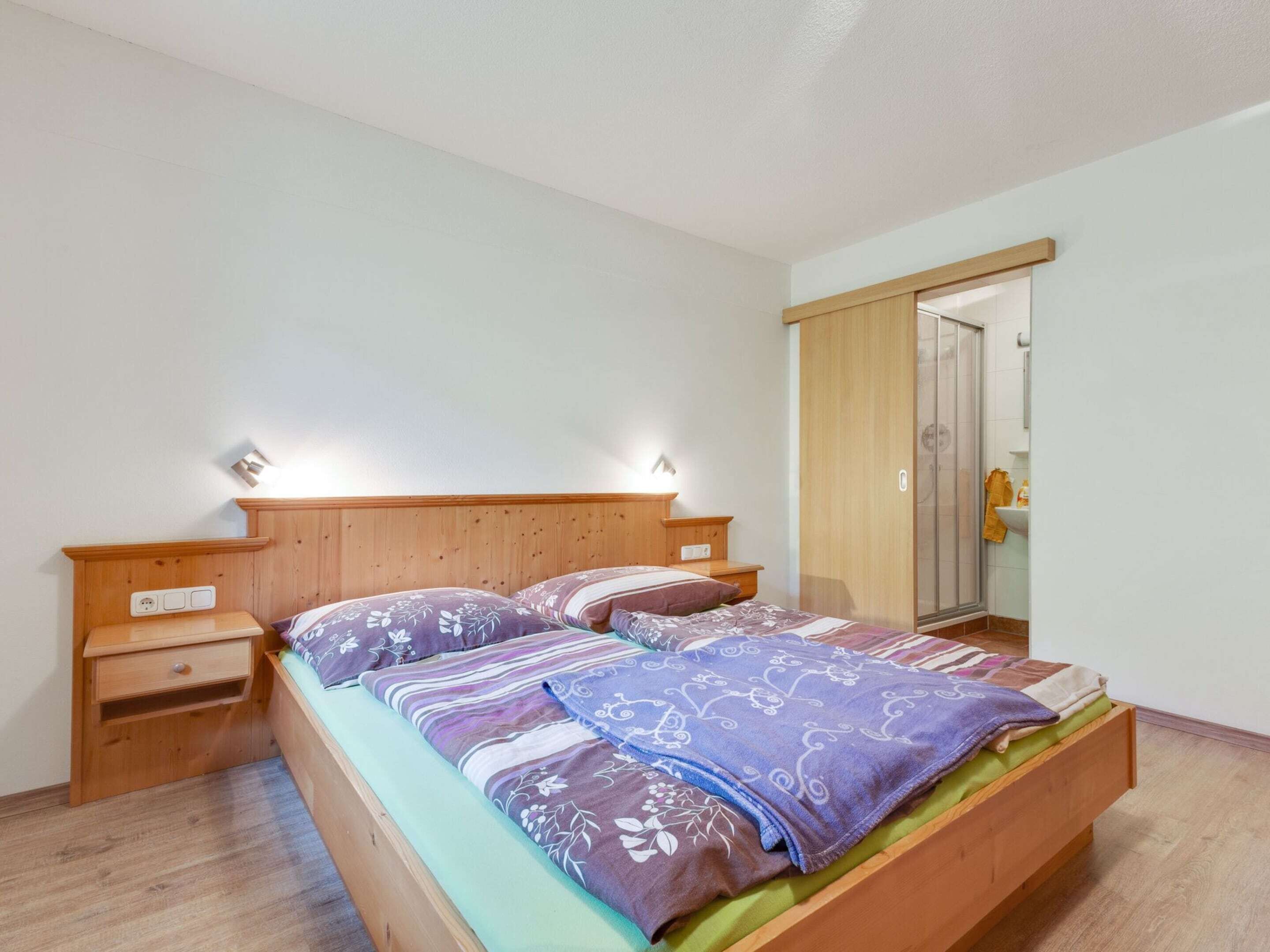 A bedroom with a wooden bed, bedside tables, a wardrobe, and a bathroom visible through a glass door.