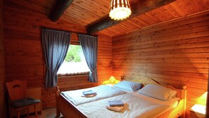 A wooden cabin room with two beds, a chair, a window with curtains, and a hanging light fixture. - Detached Holiday Residence in the Wonderfully Beautiful Harz (Osterode am Harz)