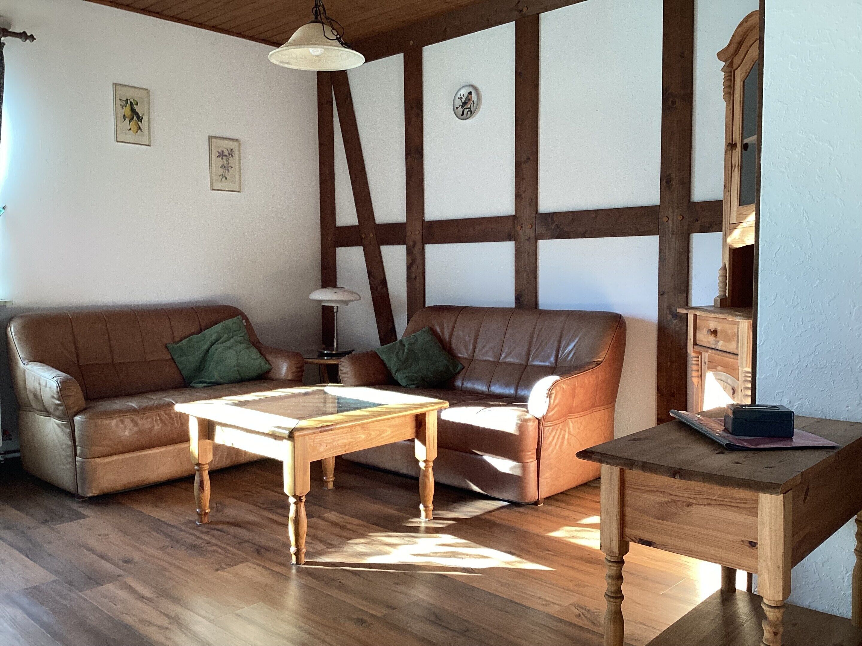 A furnished living room with a wooden floor, a brown leather sofa, a wooden coffee table, and a wooden side table.