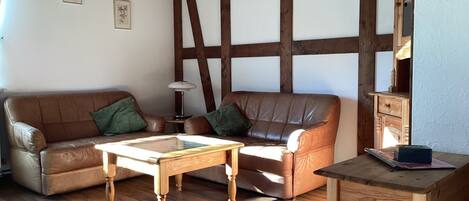 A furnished living room with a wooden floor, a brown leather sofa, a wooden coffee table, and a wooden side table.