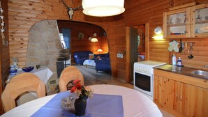 A rustic cabin interior with a stone fireplace, wooden dining table, and a kitchenette. - Detached Holiday Residence in the Wonderfully Beautiful Harz (Osterode am Harz)