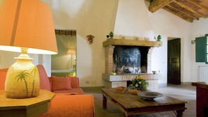 Un salon chaleureux avec une cheminée, une table sur laquelle se trouve un saladier et une lampe décorée d’un motif de palmier.