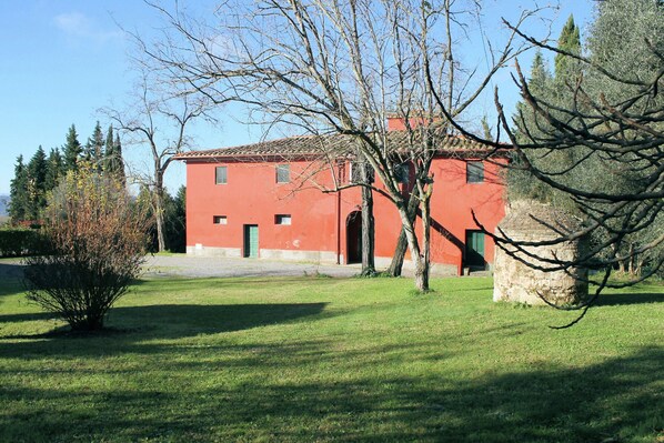 Un bâtiment rouge avec un toit en tuiles, entouré d’une pelouse et d’arbres.