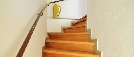 Una escalera de madera con barandilla metálica, paredes blancas y un adorno dorado en la pared.