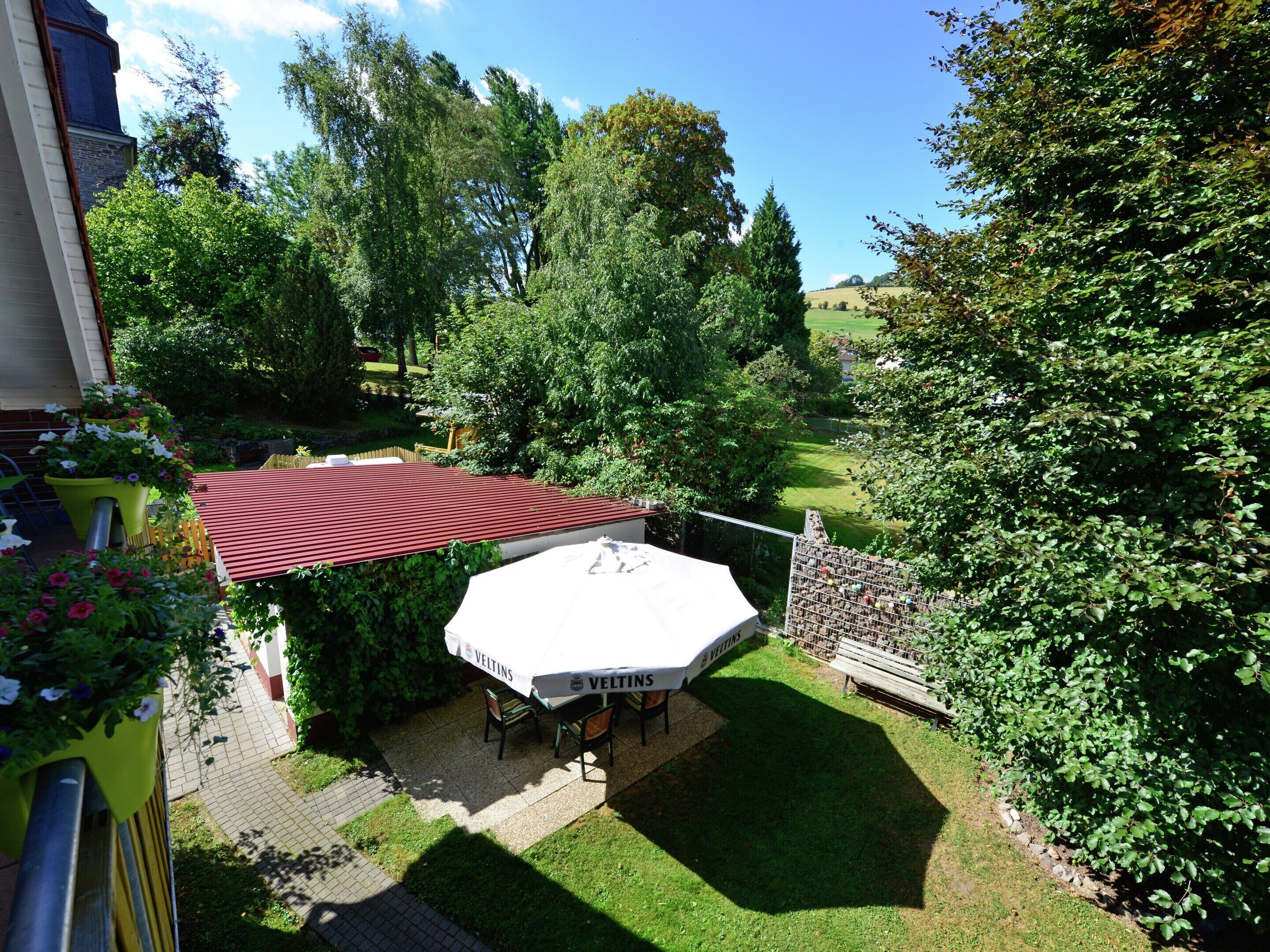 Un espace extérieur aménagé, abrité et doté de tables et de chaises, entouré d’une végétation luxuriante et offrant une vue sur un paysage rural.