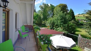 A balcony with green chairs, a white umbrella, and a view of a green landscape.